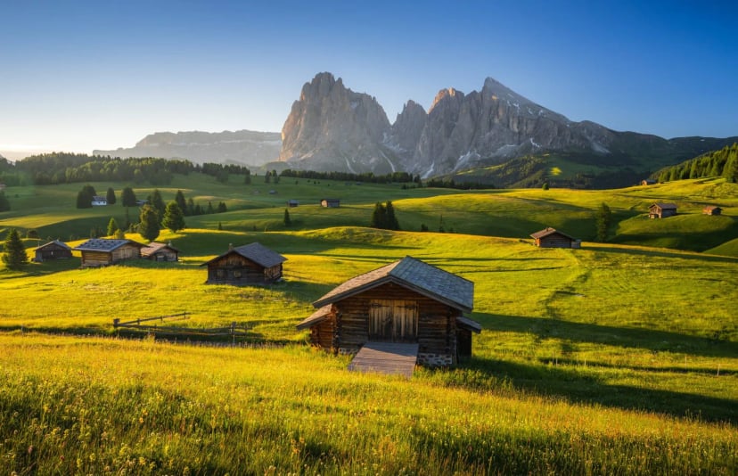 Alpine meadows with wooden huts and dramatic mountains at sunrise, Seiser Alm.