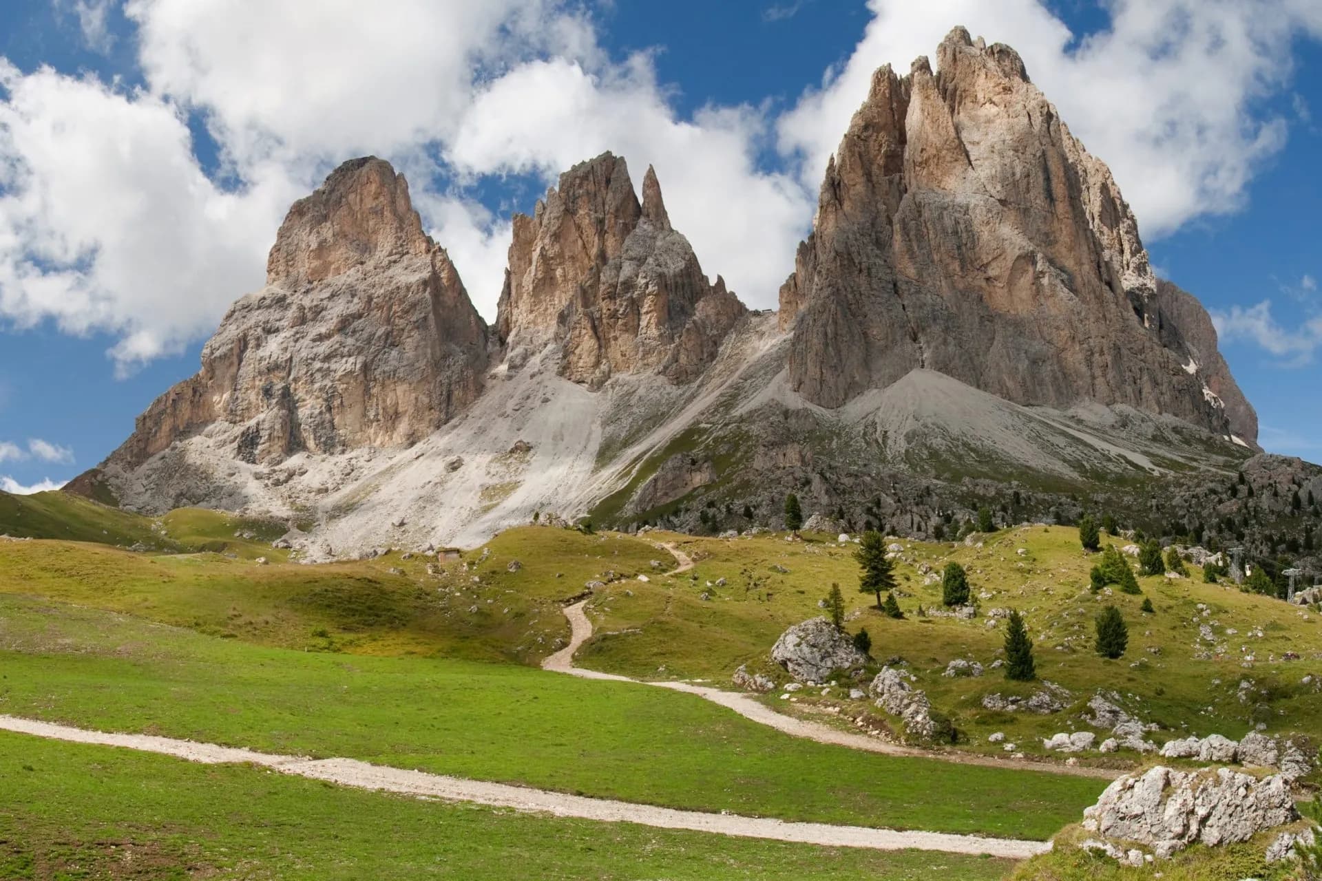 Rocky mountain peaks above green alpine meadow with winding dirt hiking path, Sella Pass.