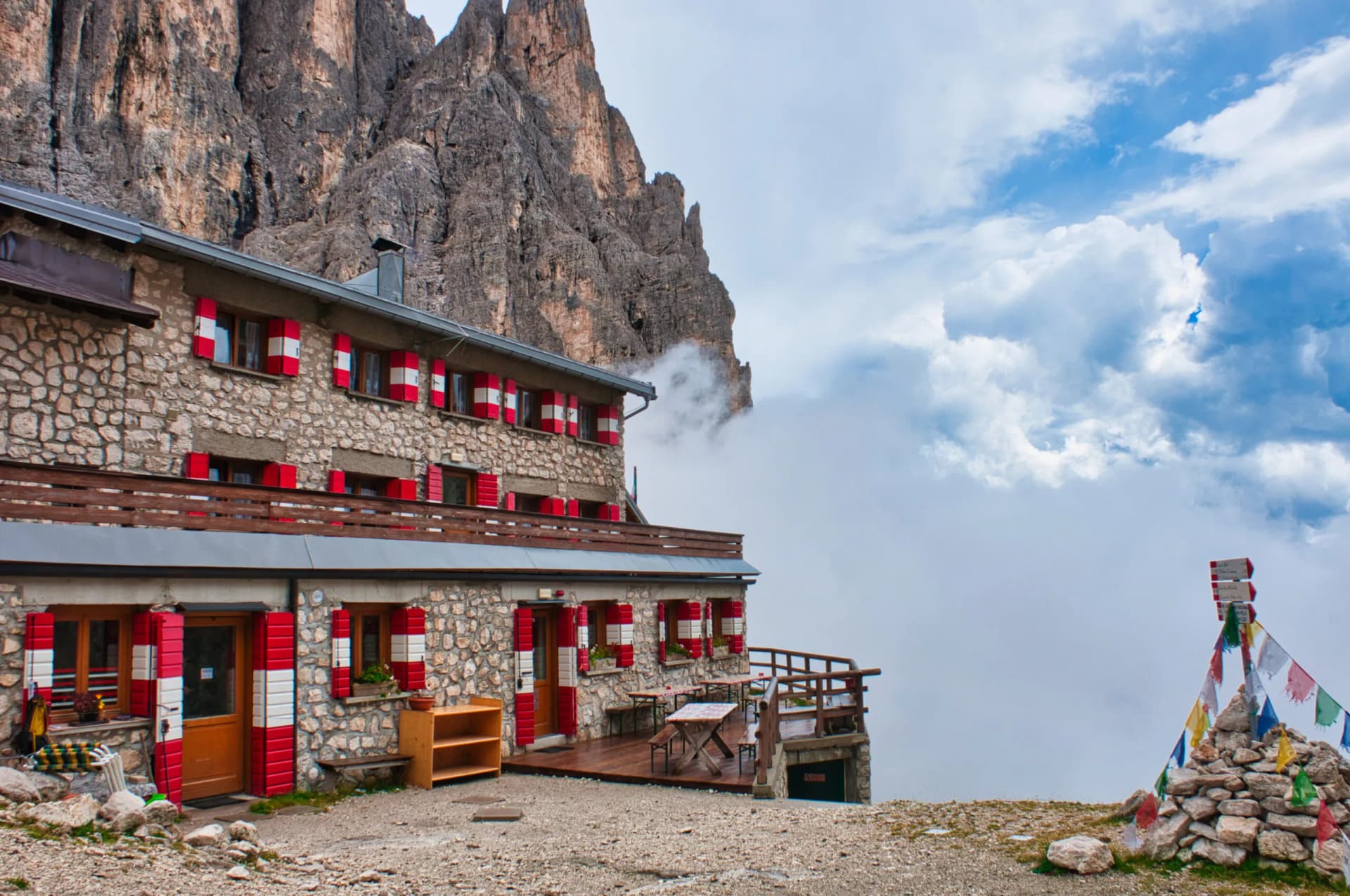 Rifugio Pradidali mountain hut with stone walls and red/white shutters against jagged peaks and clouds.