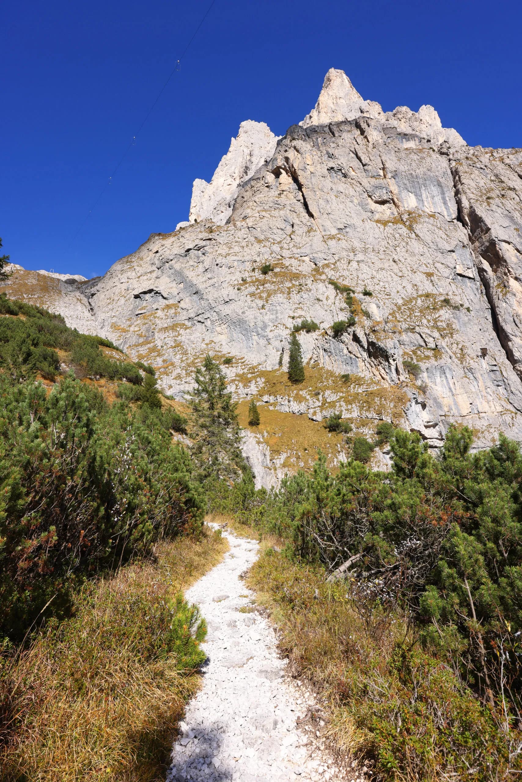 Hiking path leading toward sheer rocky mountain peaks under a clear blue sky near Rifugio Pradadali.
