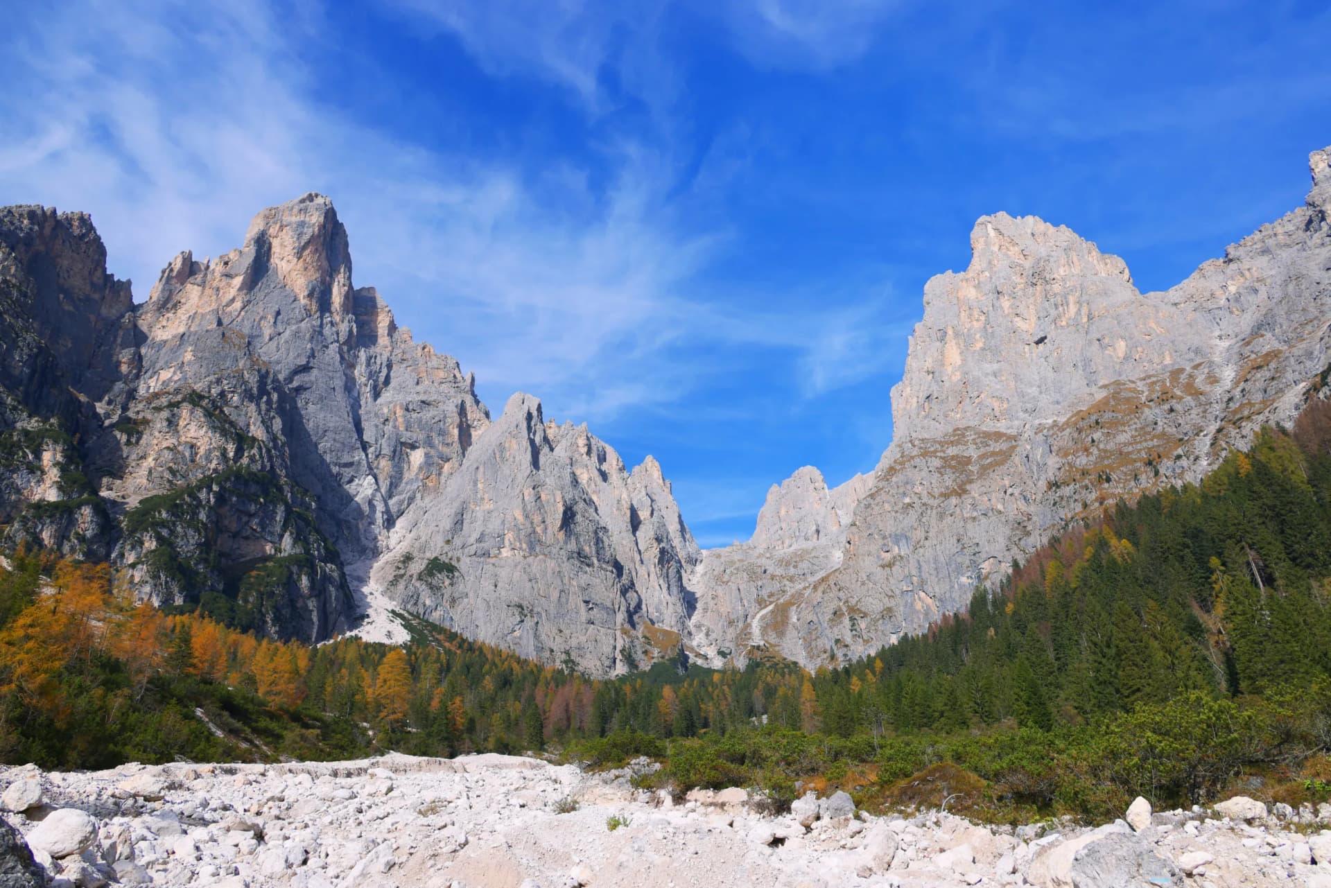 Rocky ascent toward Rifugio Treviso beneath towering gray Dolomite peaks in autumn.