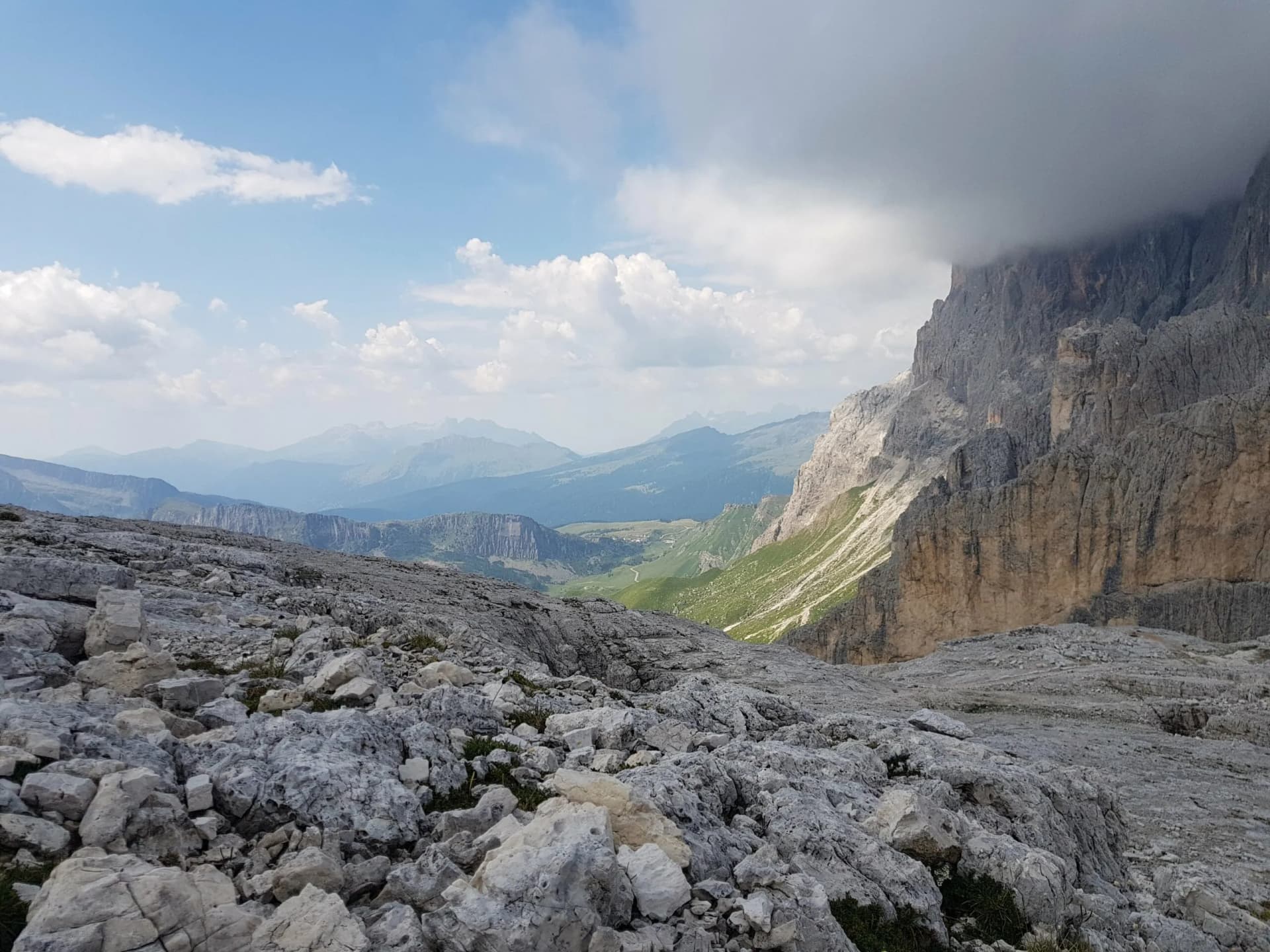 Hiking over rocky terrain with views of towering cliffs and distant green valleys in Pale di San Martino.