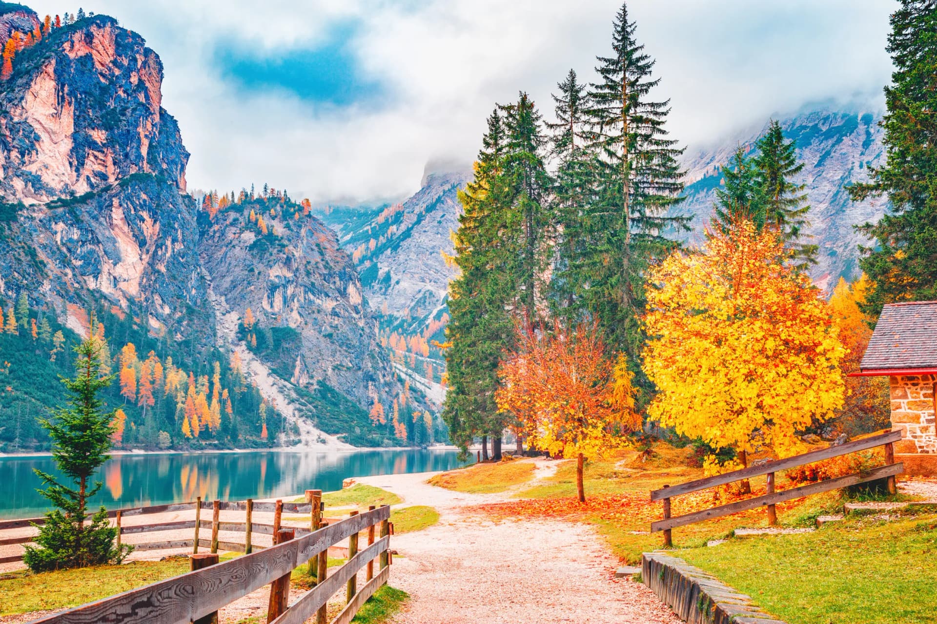 Hiking path near Lago di Braies with autumn foliage, mountains, and a stone building.