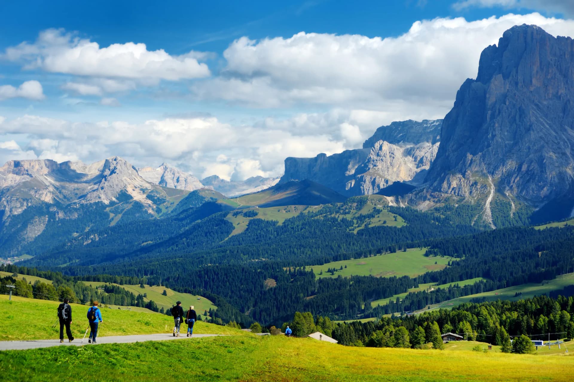 Hikers walking on path with vast alpine meadows and dramatic mountains in Seiser Alm