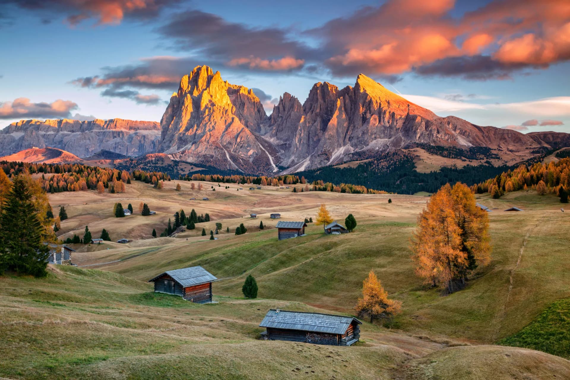 Seiser Alm alpine meadow with wooden huts and rugged mountains at sunset in autumn