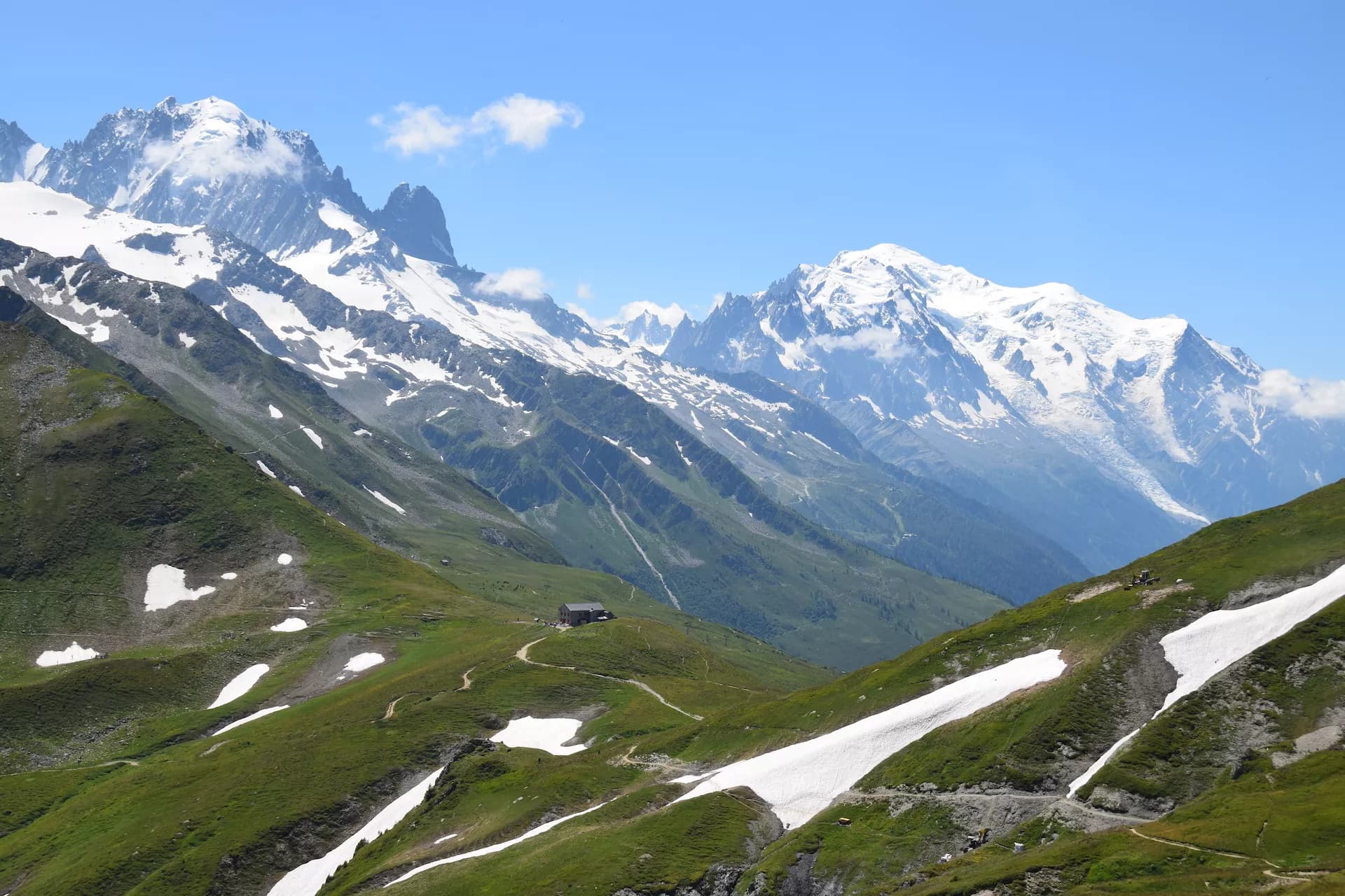 Col de Balme mountain pass with green slopes, snow patches, and Mont Blanc in the background.