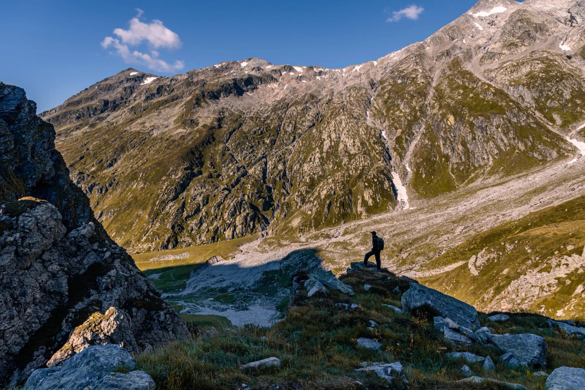 Majestic alpine landscape in the Lord of the Rings style near the Scaletta hut. In the foreground is a grassy expanse with a path running across it towards the high mountains in the background, which