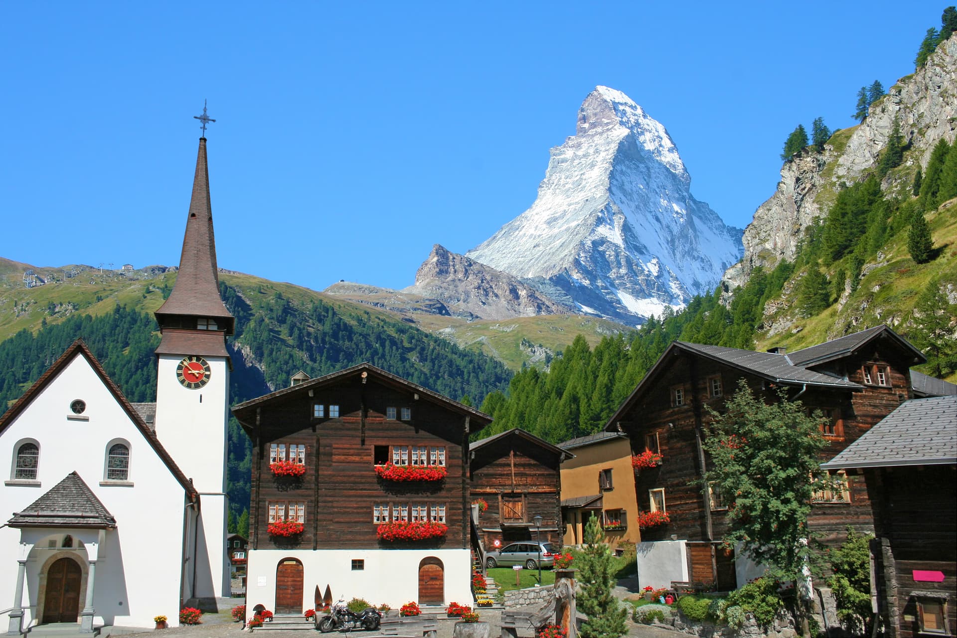 Alpine village with wooden chalets, a church, and the snow-capped Matterhorn mountain.
