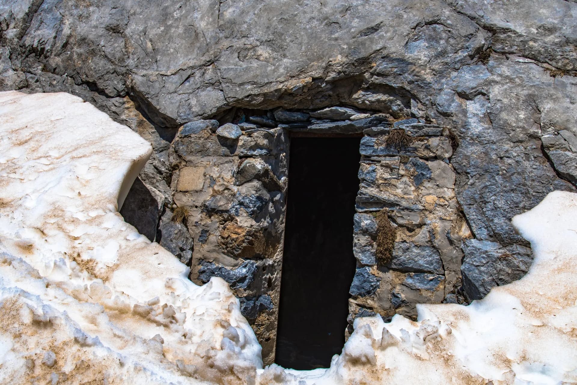 Stone entrance built into a rock face next to melting, dirty snow, likely Bellevue Cave.