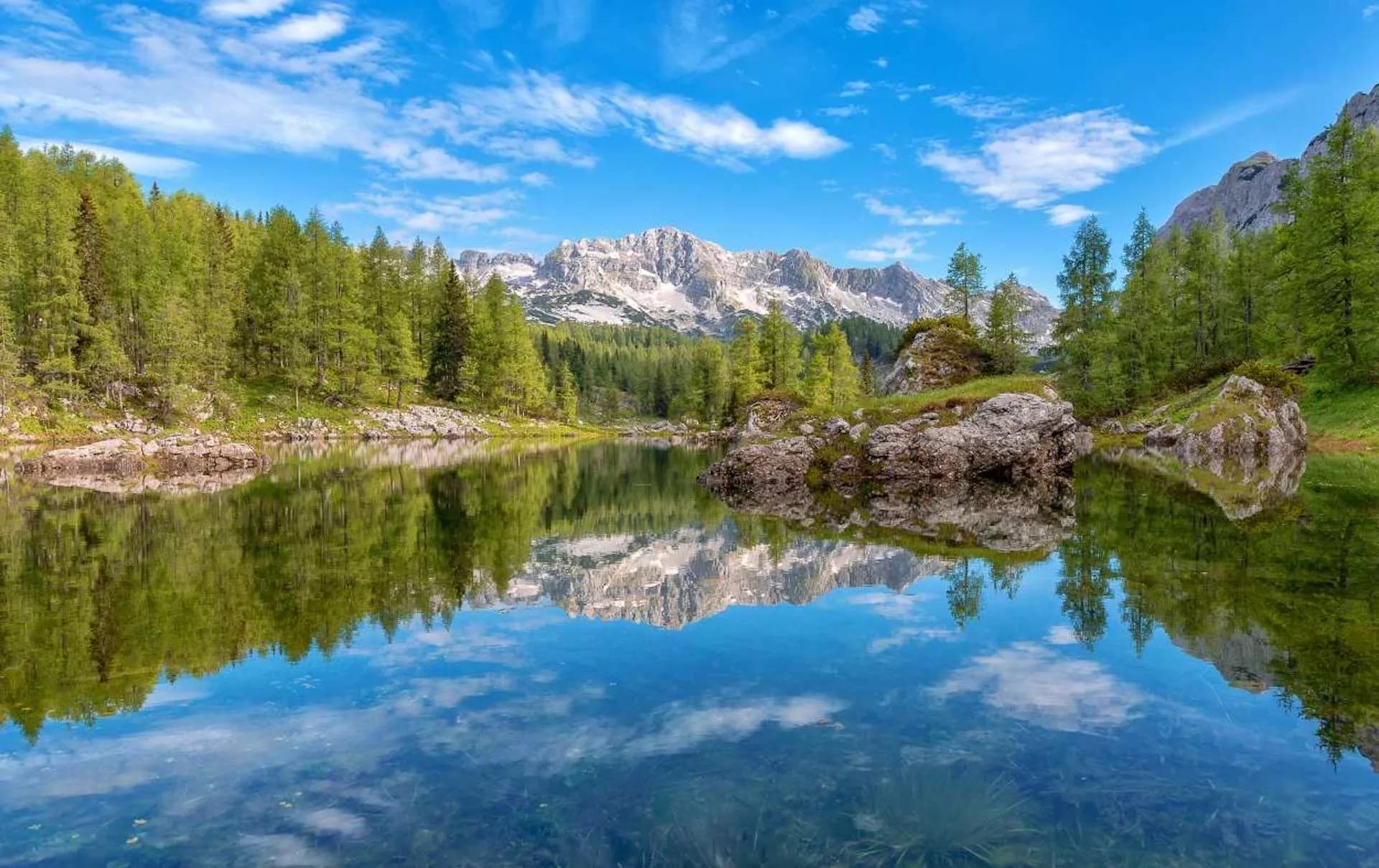 Mountain reflection on clear lake surrounded by green forest under blue sky, Valley of the Seven Lakes.