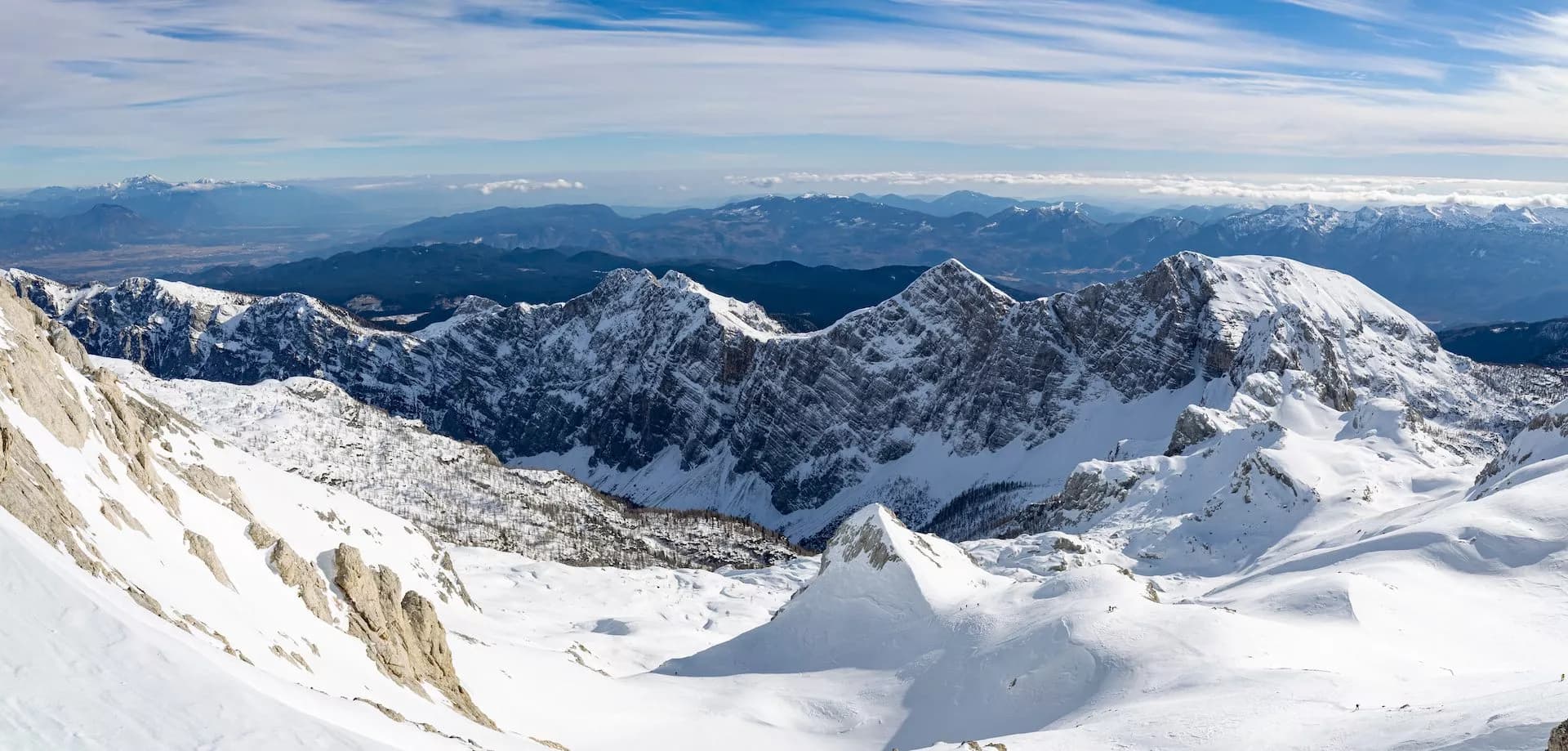Snowy alpine mountain range view from Kredarica in winter with distant valleys under blue sky.