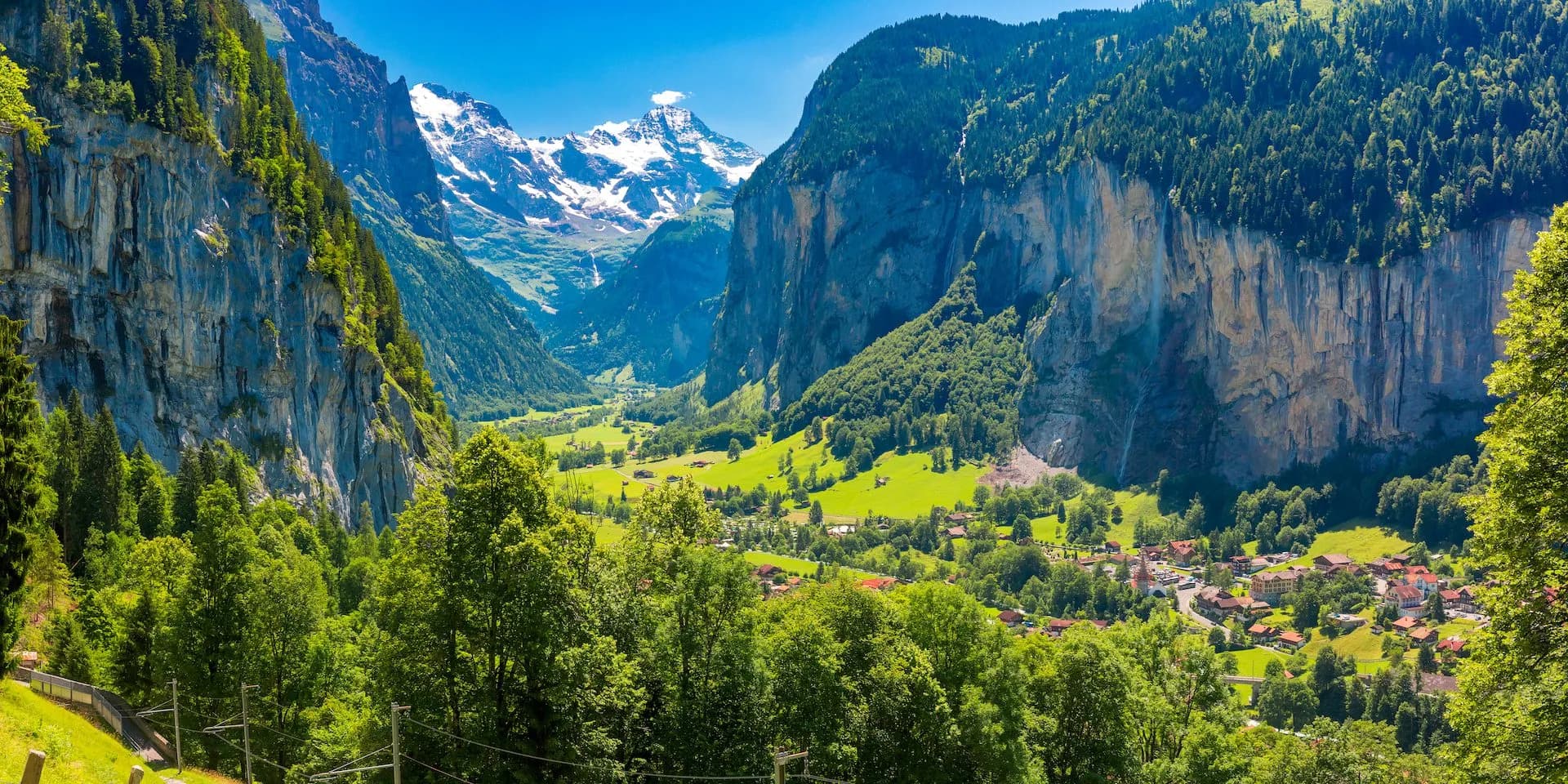 Lauterbrunnen Valley with sheer cliffs, green meadows, village, and snow-capped mountains.