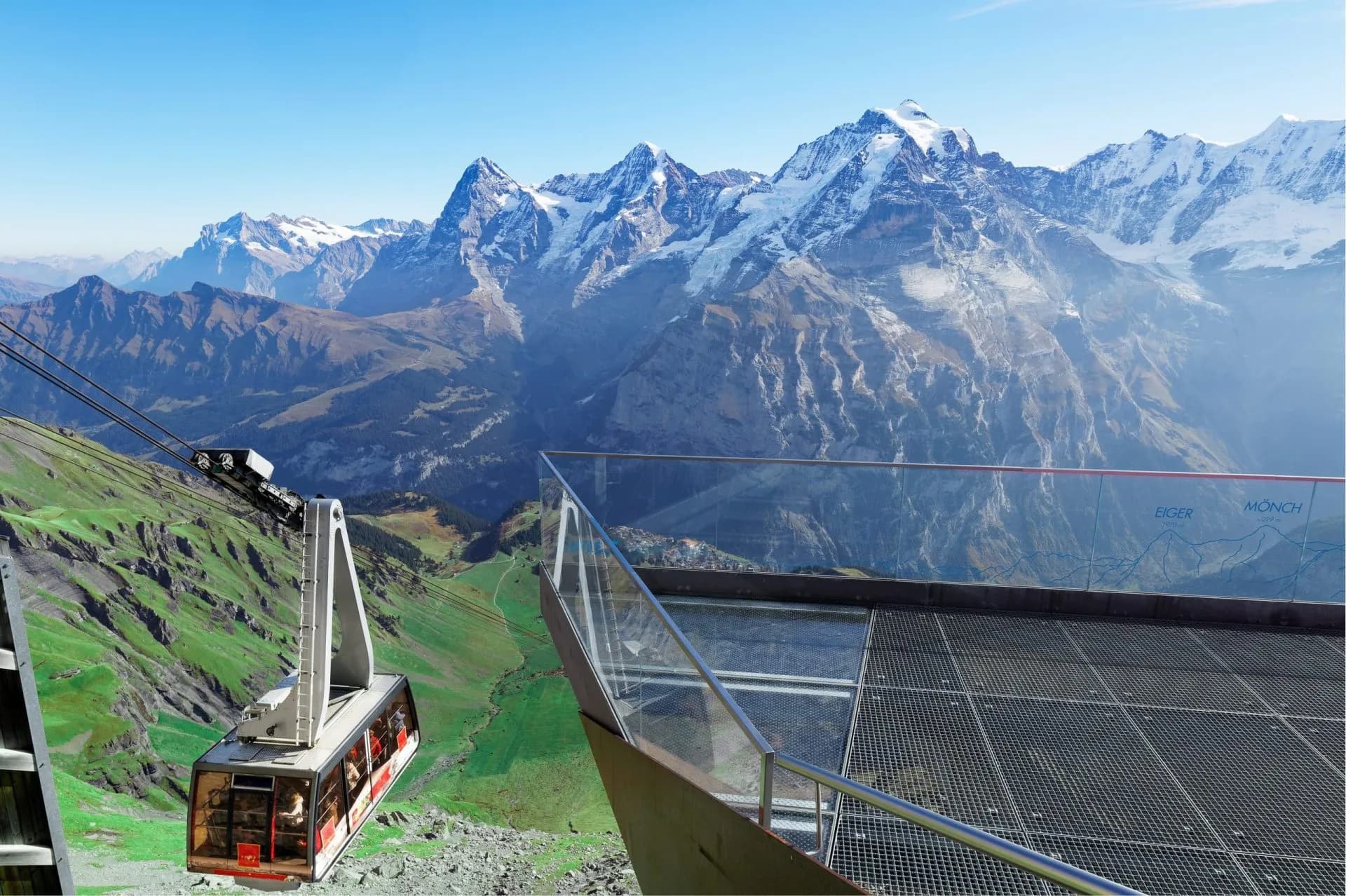 Cable car ascending past viewing platform with Eiger and Mönch snow-capped mountains