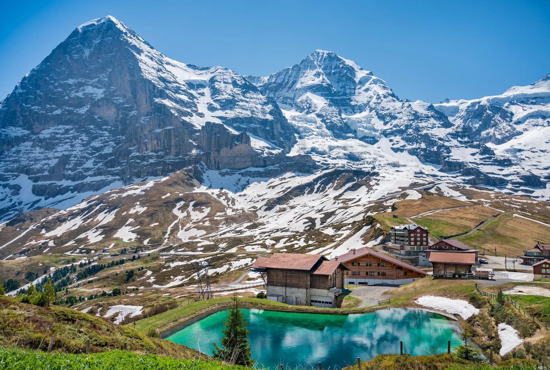 Kleine Scheidegg with Eiger North Face, snow-capped mountains, and turquoise pond in foreground.